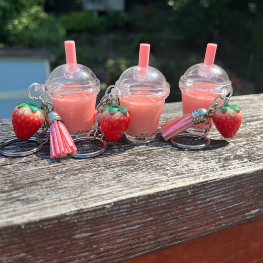 Three Boba tea keychains filled with pink resin, black boba pearls, and plastic strawberries and tassels attached